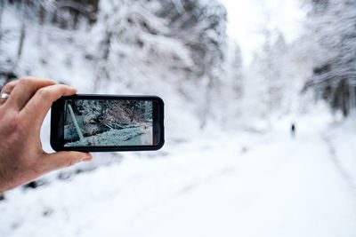 Midsection of person photographing with smartphone in snow covered landscape