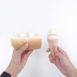 Cropped image of woman holding ice cream cone and sandwich against white background