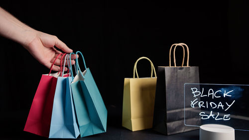 Cropped hands of woman holding shopping bags against black background