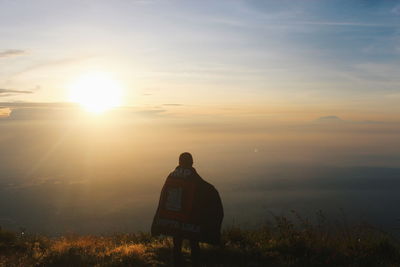 Rear view of person standing on field against sky during sunset