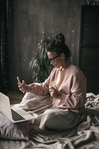 Young woman using mobile phone while sitting on bed