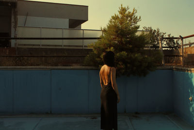 Rear view of woman standing by swimming pool against building