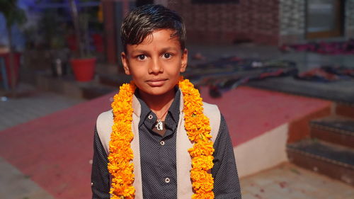 Cute and innocent asian boy with yellow flowers garland looking at cameraman.