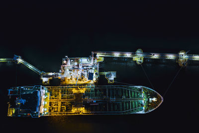 Illuminated factory by sea against clear sky at night