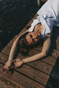 High angle portrait of young woman lying on pier over lake