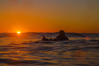 Silhouette woman swimming in sea against clear orange sky