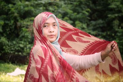 Portrait of young woman standing against trees