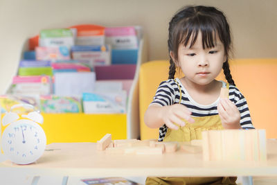 Cute girl playing with toy blocks on table at home