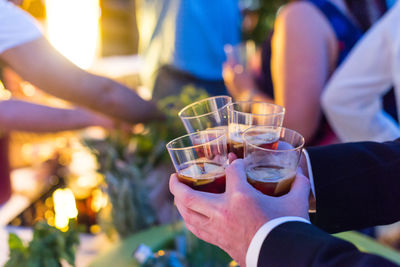 Cropped hands of man holding drinks by friends during party