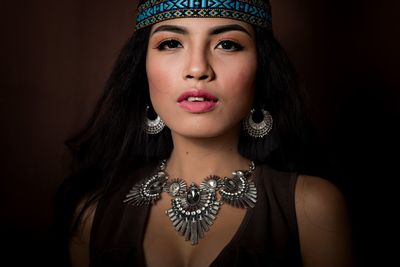 Close-up portrait of beautiful young woman wearing jewelries against black background