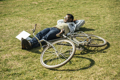 Young man with bicycle, relaxing, lying on grass