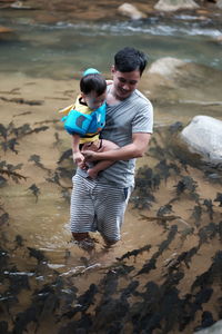 Father holding his son while standing amidst fish swimming in river