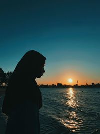 Silhouette girl standing at beach against clear sky during sunset