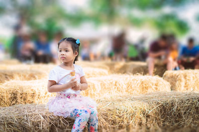 Cute girl eating ice cream while looking away on hay