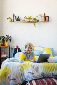 Portrait of happy mid adult woman using laptop while lying on bed at home