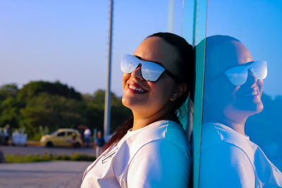 Smiling woman wearing sunglasses while leaning on wall