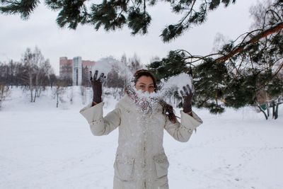 Young woman throwing snow while standing on land during winter