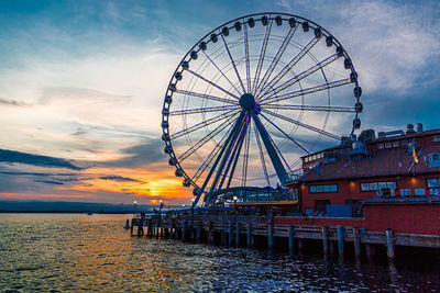 Ferris wheel by sea against sky during sunset