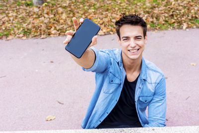 Portrait of smiling man showing mobile phone in city