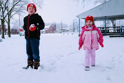 Full length portrait of boy and girl playing while standing in snow