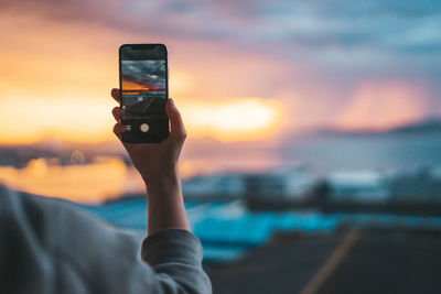 Man photographing through smart phone against sky during sunset