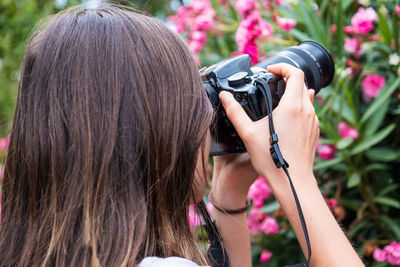 Close-up of woman photographing flowering plants with digital camera in park