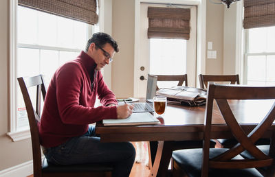 Man in glasses working from home using a computer at a dining table.