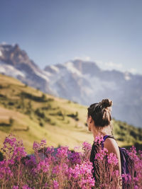 Rear view of woman walking on purple flowering plants against sky