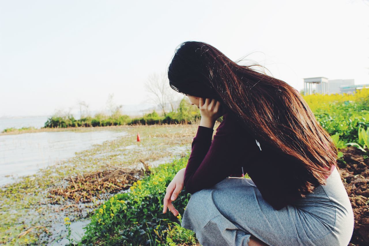 lifestyles, long hair, young adult, leisure activity, young women, casual clothing, clear sky, sitting, side view, waist up, rear view, person, water, relaxation, nature, three quarter length, tranquility