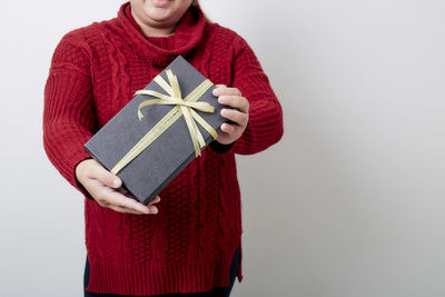 Midsection of woman wearing sweater holding gift while standing against white background