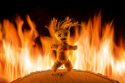 A needle punched voodoo doll stands in front of a bright fire