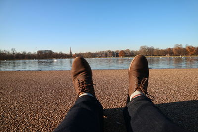 Low section of man standing by lake against clear sky