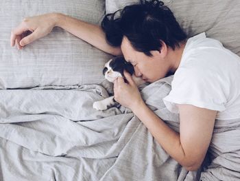 High angle view of young man with kitten sleeping on bed at home