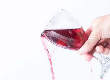 Close-up of hand holding red wine against white background