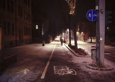 Mid distant view of person walking on illuminated bicycle lane in city at night