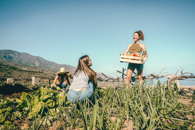 Smiling woman talking with friend picking vegetables in farm