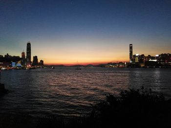 Scenic view of river by illuminated buildings against sky during sunset