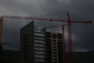 Low angle view of crane by building against sky