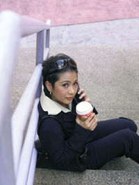 High angle portrait of businesswoman holding disposable cup while using smart phone on steps