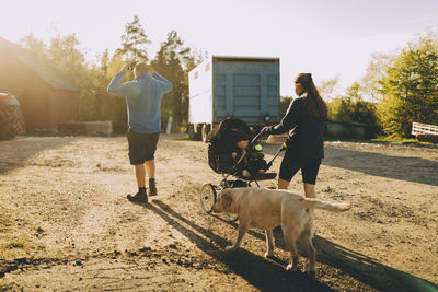 Parents with male toddler walking by dog on sunny day