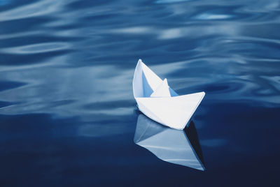 Single white paper boat floating in the blue sea