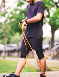 Blurry photo of a bearded man using jumping rope outdoors and looking at his smart watch.