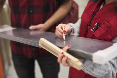 Midsection of saleswoman marking with pencil on metal plank while standing with customer in hardware store