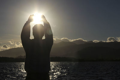 Silhouette man standing by lake against mountains during sunset