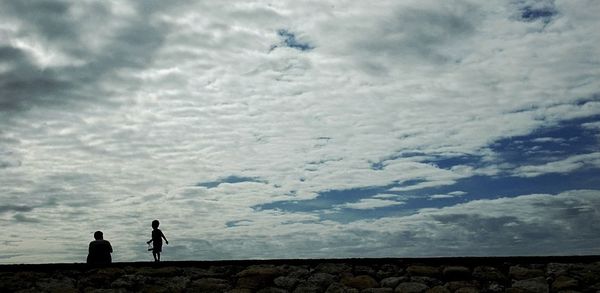 Silhouette of people standing on landscape against cloudy sky