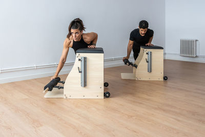 Female athlete doing exercises on pilates chair under supervision of personal instructor during workout in gym