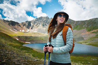 Smiling, positive girl with disheveled hair against the background of a blue mountain lake, with