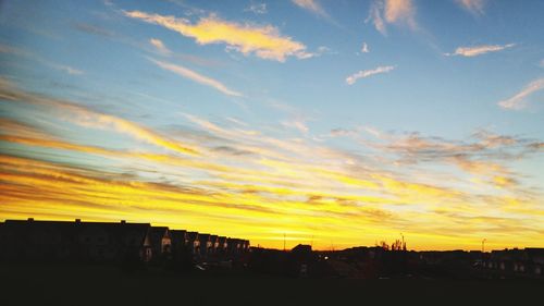 Silhouette of city against cloudy sky during sunset