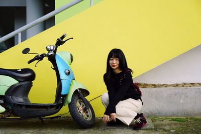 Portrait of woman by motor scooter against yellow wall