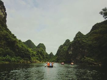 People on river amidst trees against sky